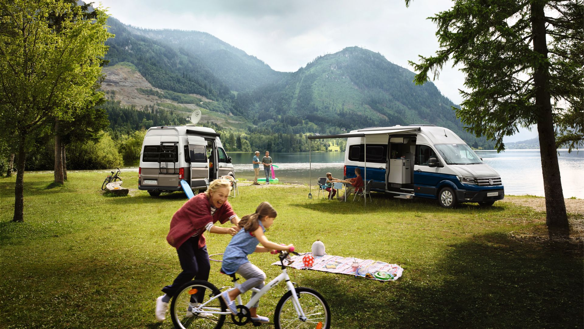 VW Grand California blanc et bleu, vue latérale avec une famille au bord d'un lac