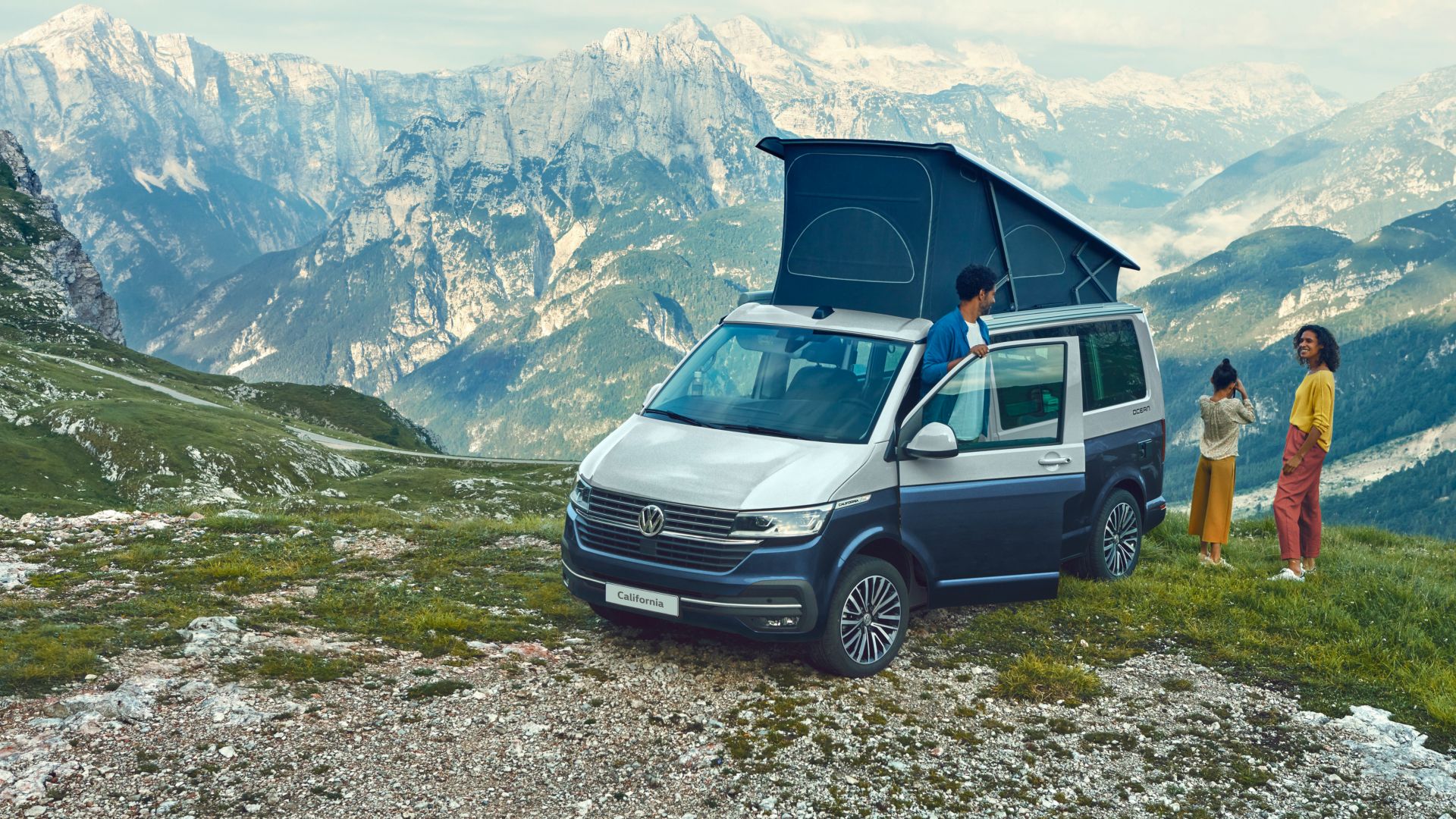 Grey and blue VW California Ocean with pop-up roof front and side view in mountain scenery
