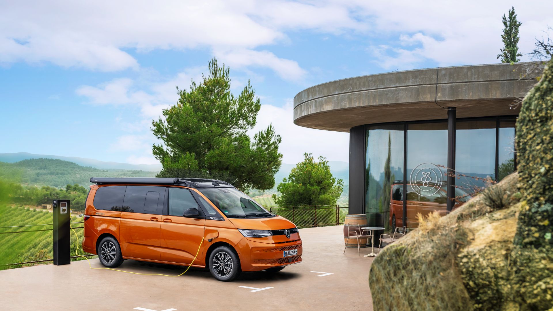 Vista laterale del VW California eHybrid arancione in un parcheggio