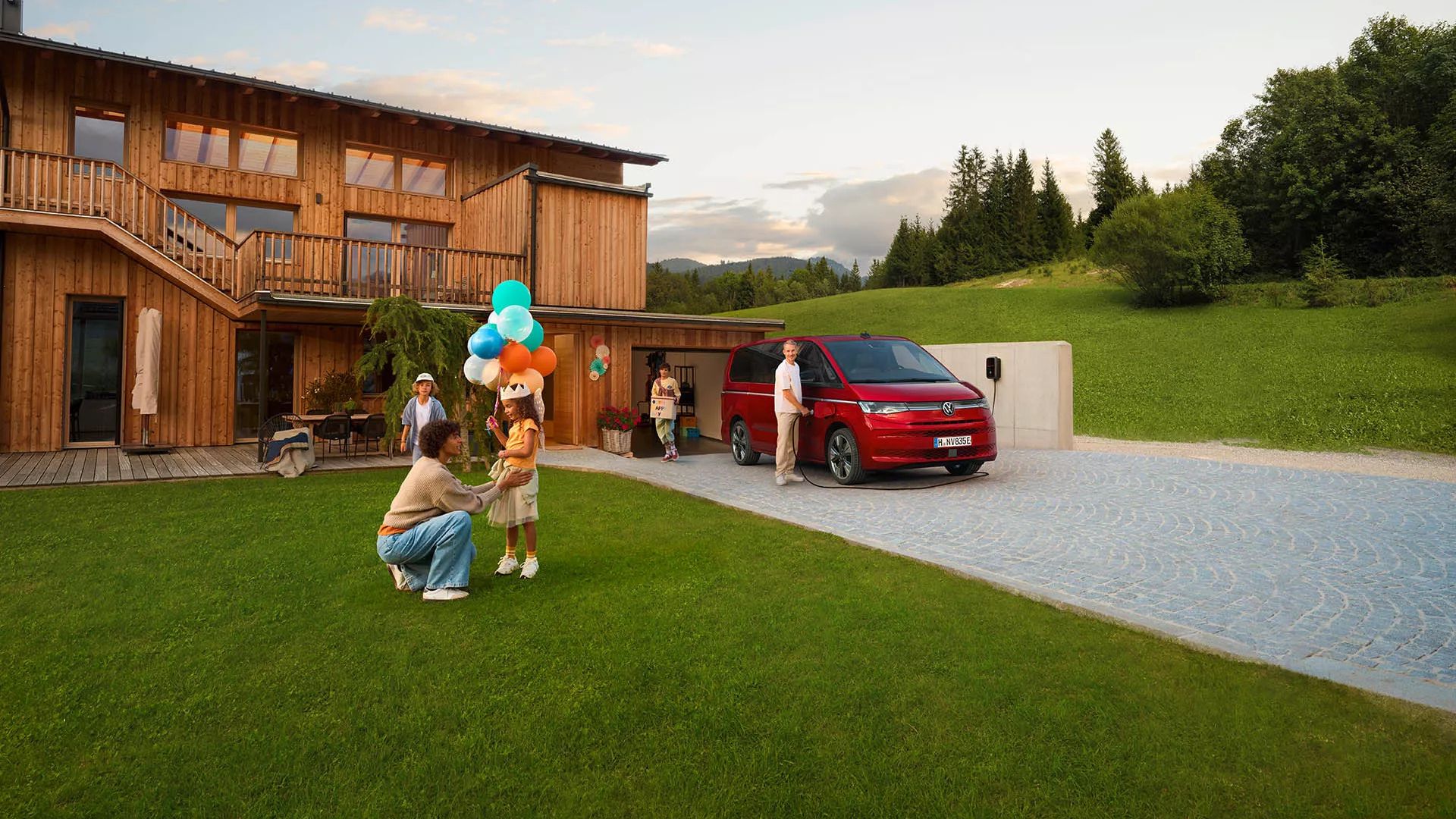 VW Multivan rouge vu de face avec une famille devant une maison