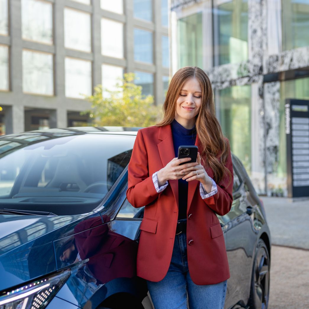 Application AMAG Femme avec téléphone portable devant une voiture