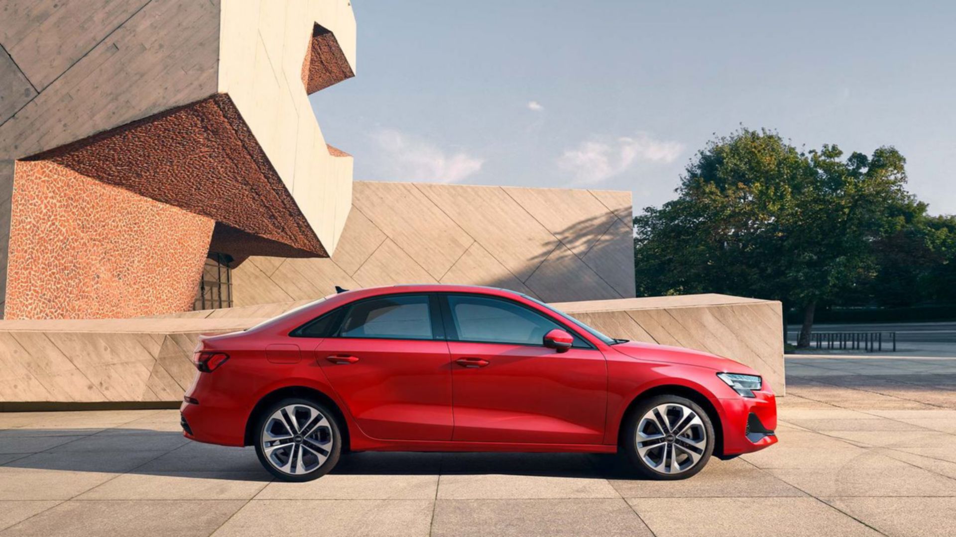 Red Audi A3 saloon side view in front of a building