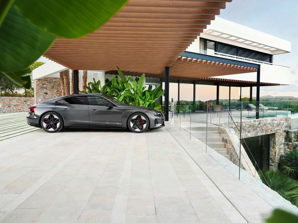 Grey Audi e-tron GT side view with a man standing next to it and a city in the background