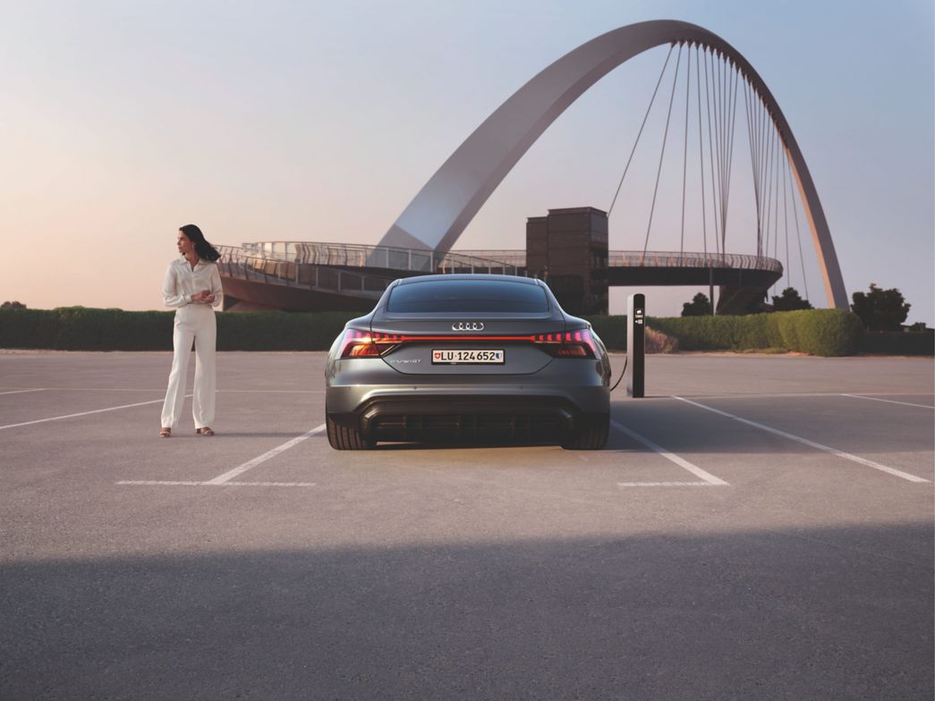 Geparkter, grauer Audi e-tron GT Heckansicht mit einer Frau daneben und einer Brücke im Hintergrund