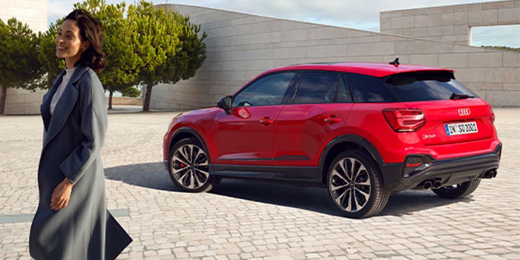 Audi SQ2 rouge vue latérale dans la ville avec femme à côté