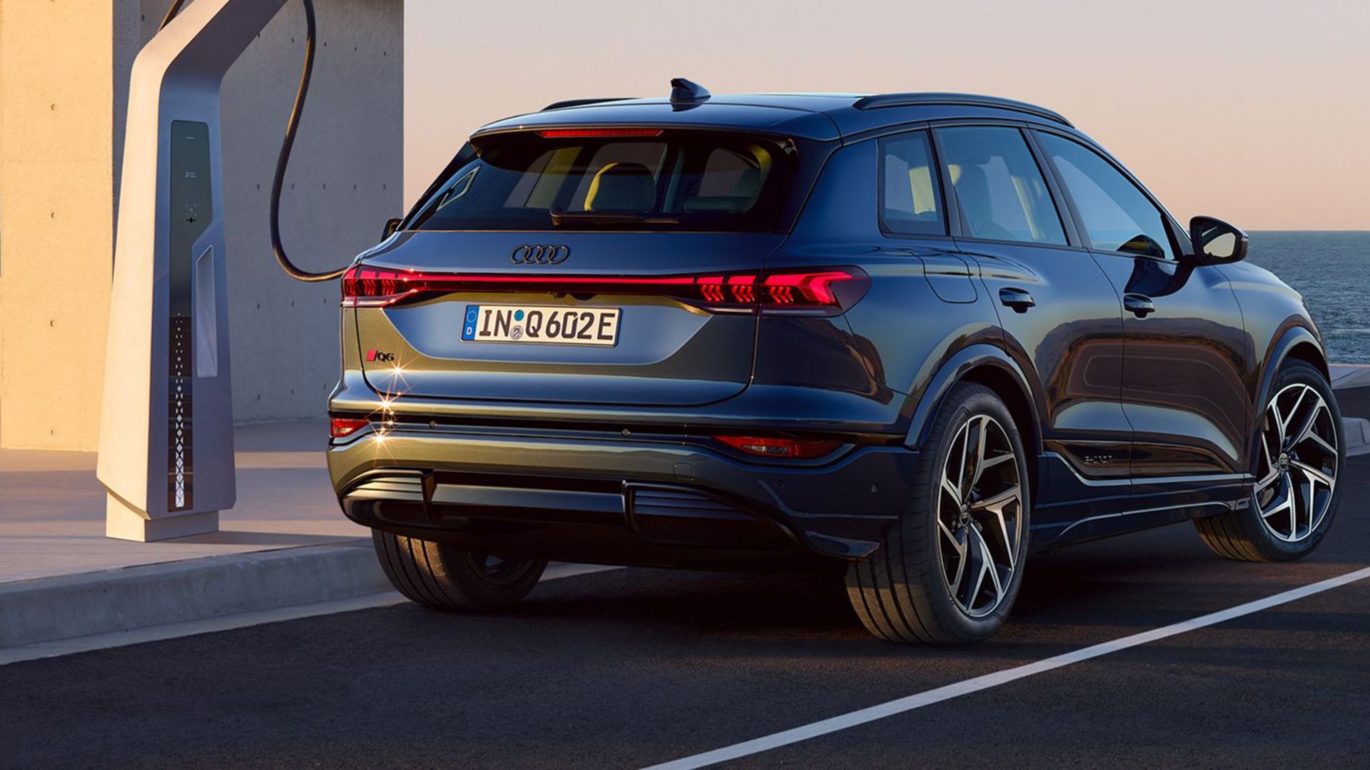 Audi Q6 e-tron visto posteriore e laterale accanto alla stazione di ricarica