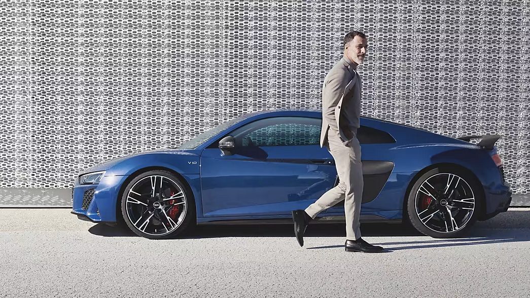 Audi R8 blu davanti al muro della griglia e uomo accanto ad essa