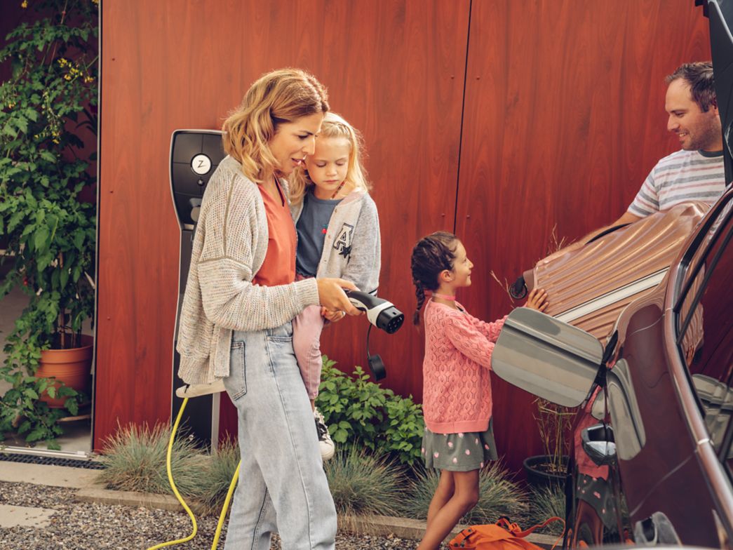 Mutter steckt Ladekabel in E-Fahrzeug