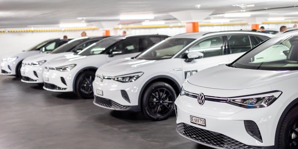 Blaues VW Elektroauto Seitenansicht und gelbes VW Elektroauto Frontansicht vor einem Gebäude