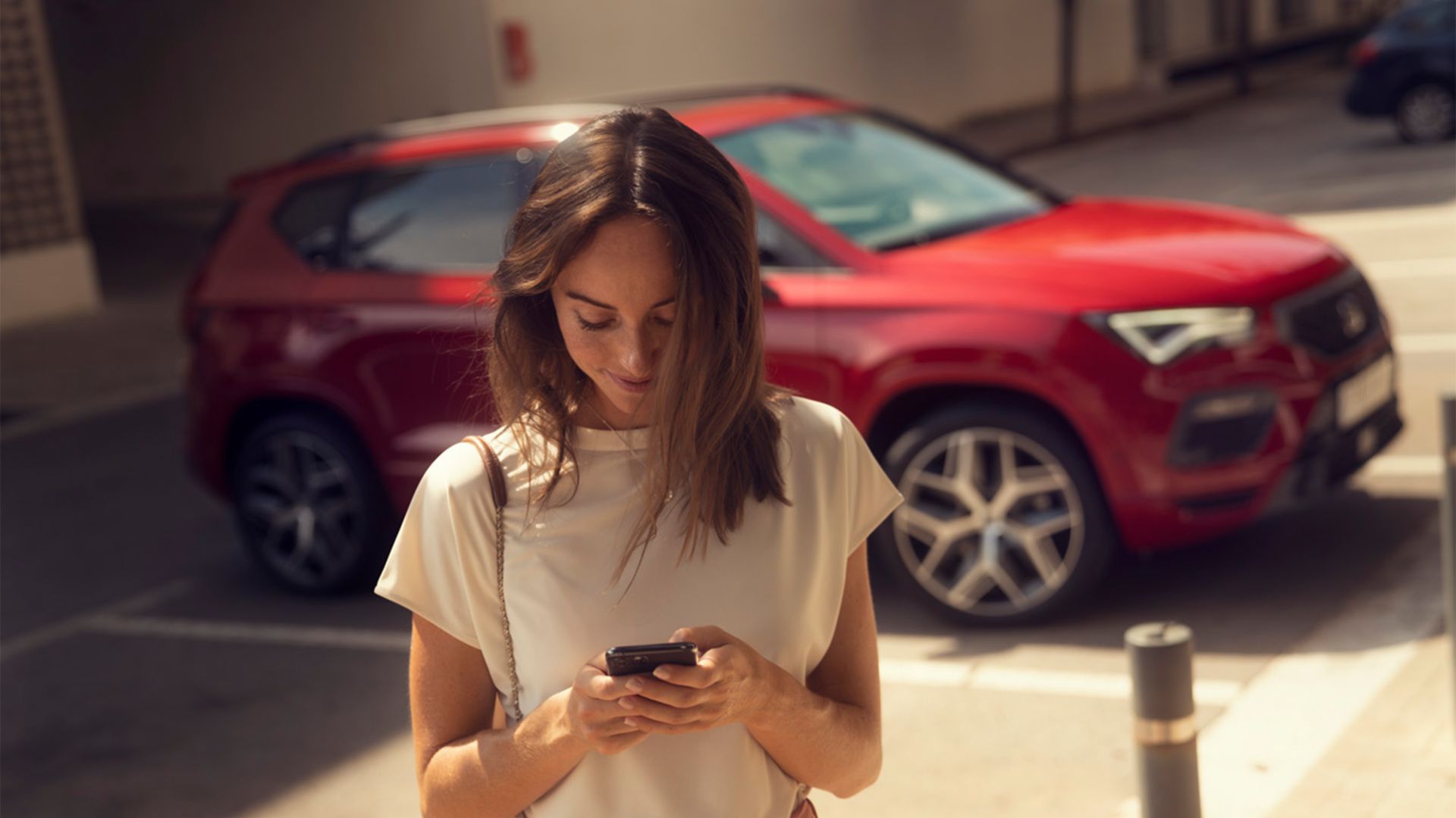 Frau mit Handy neben rotem SEAT Ateca