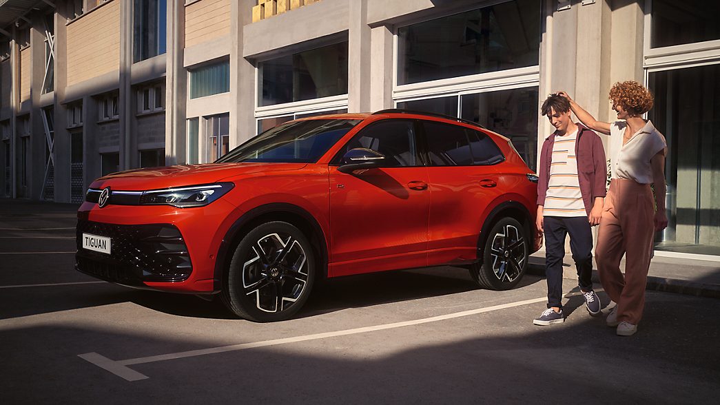 Mother and son standing next to red Tiguan in side view