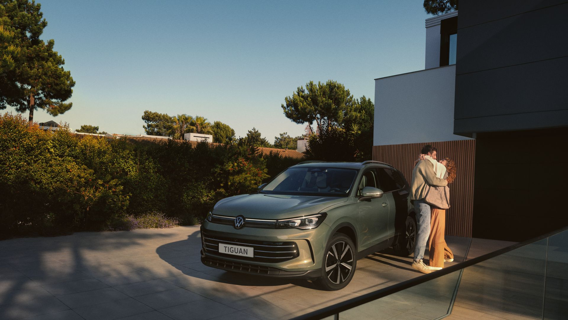 Paar umarmt sich neben grünem VW Tiguan in Front/-Seitenansicht