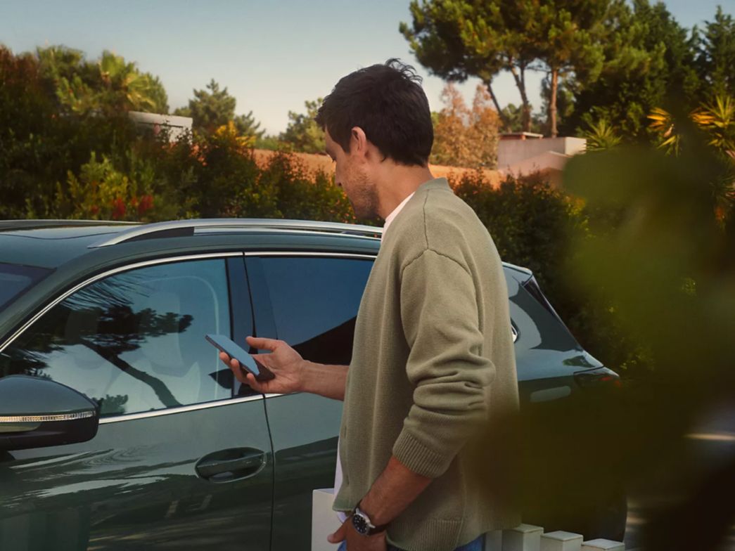 Mann steht vor VW Tiguan mit Smartphone in der Hand