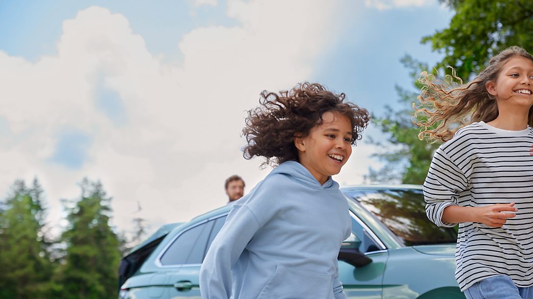 Zwei Kinder laufen lachend bei parkendem neuen VW Passat 