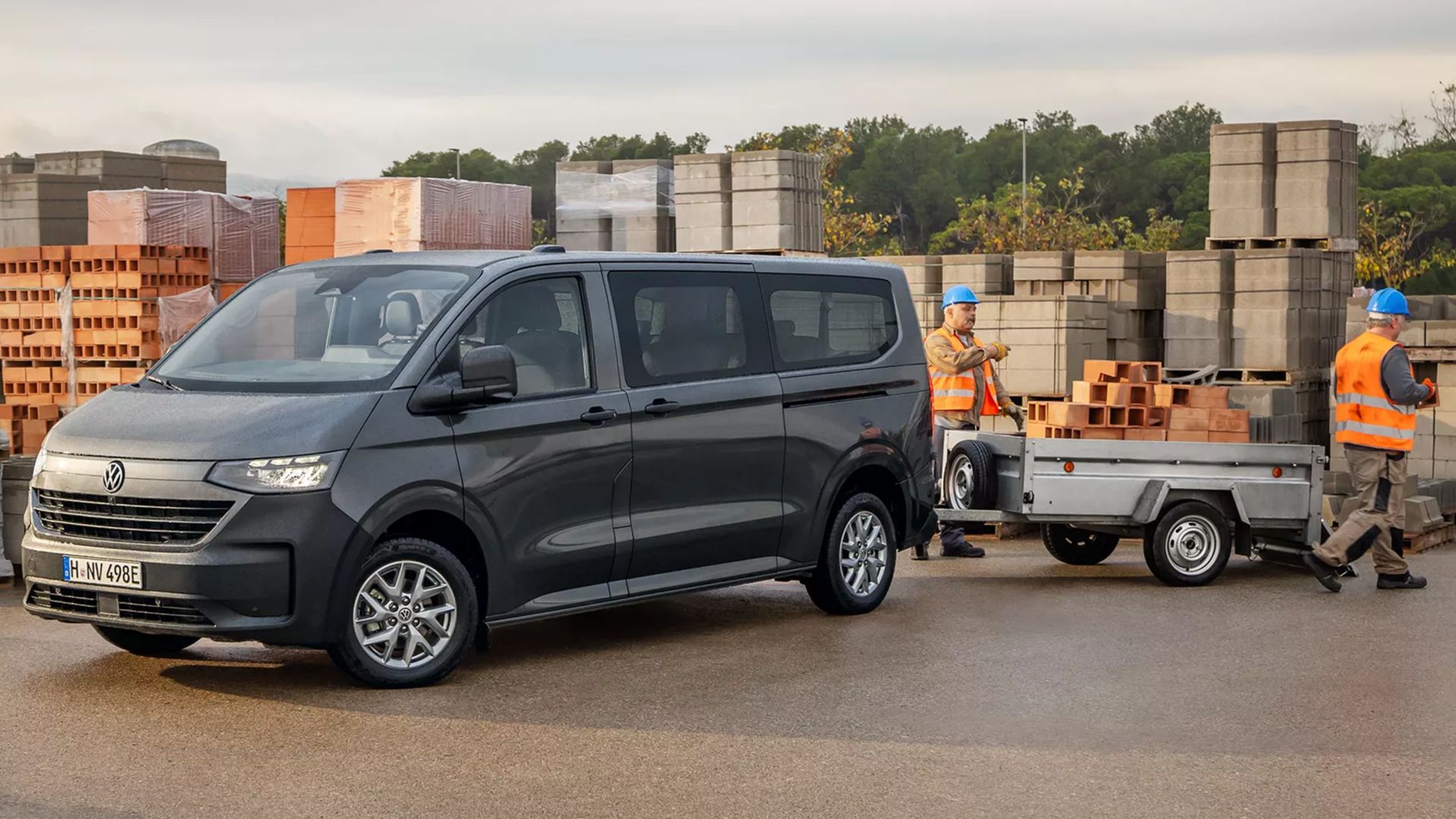 VW Transporter gris vue latérale avec une remorque et des ouvriers