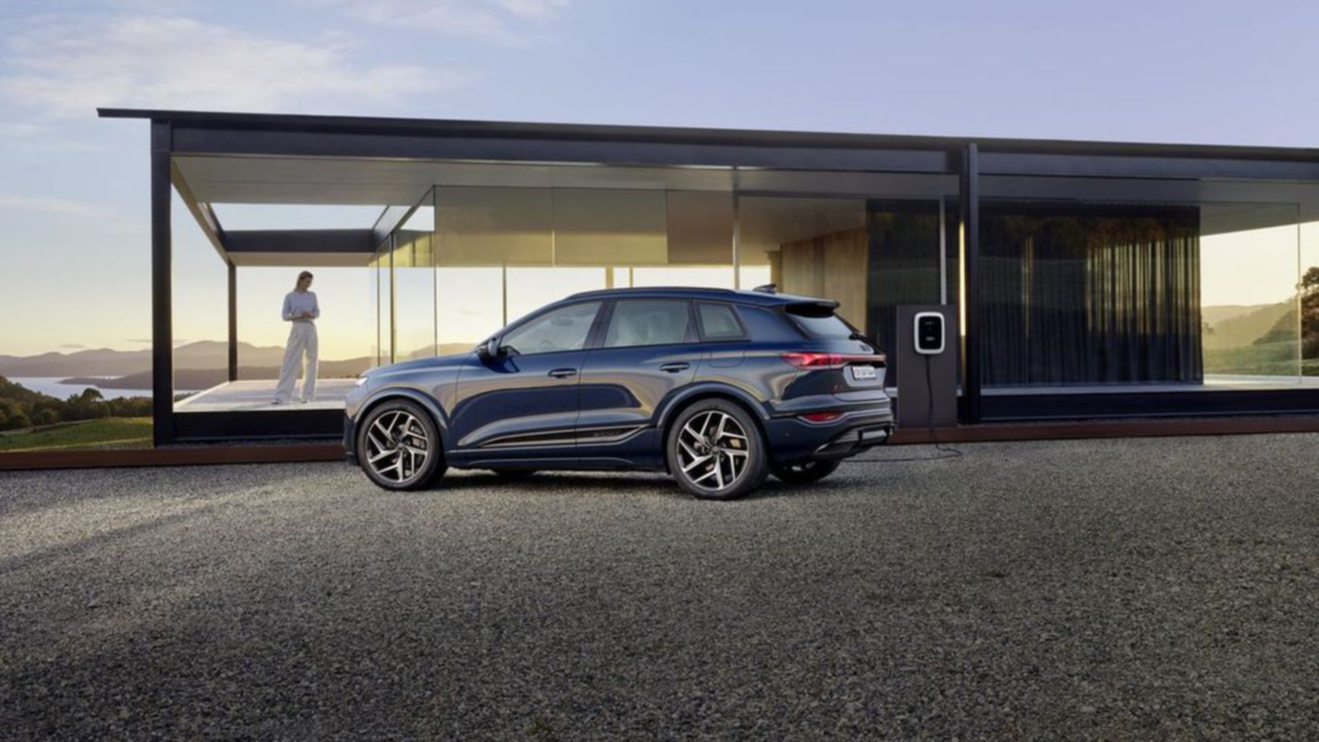 Blue Audi Q6 e-tron side view parked next to a house with glass front