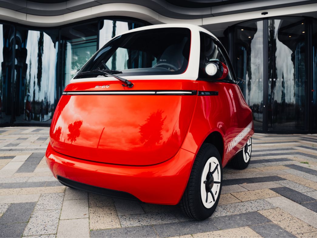 Red Microlino in front of a building front view
